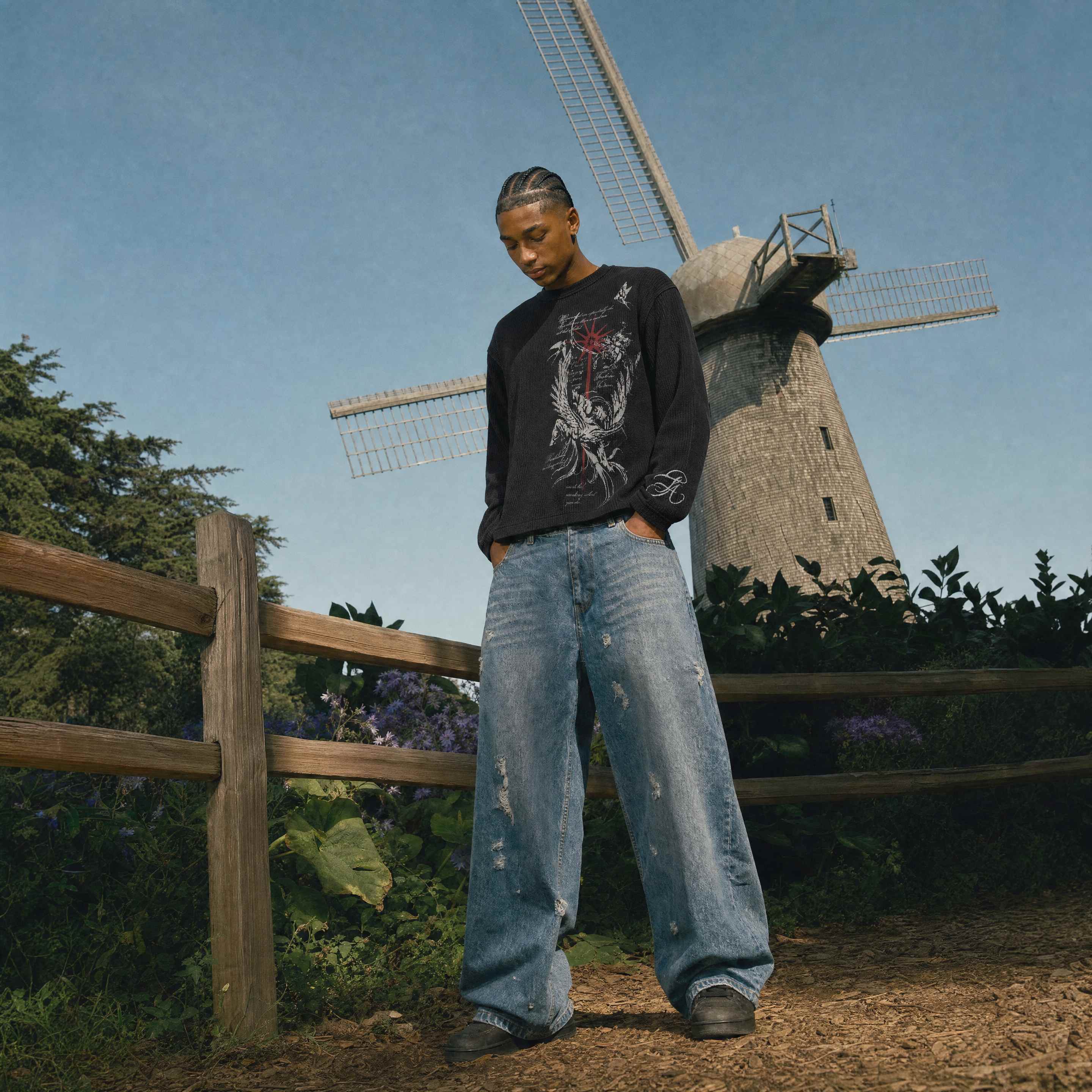 Model in a black graphic long-sleeve and baggy jeans standing in front of a windmill