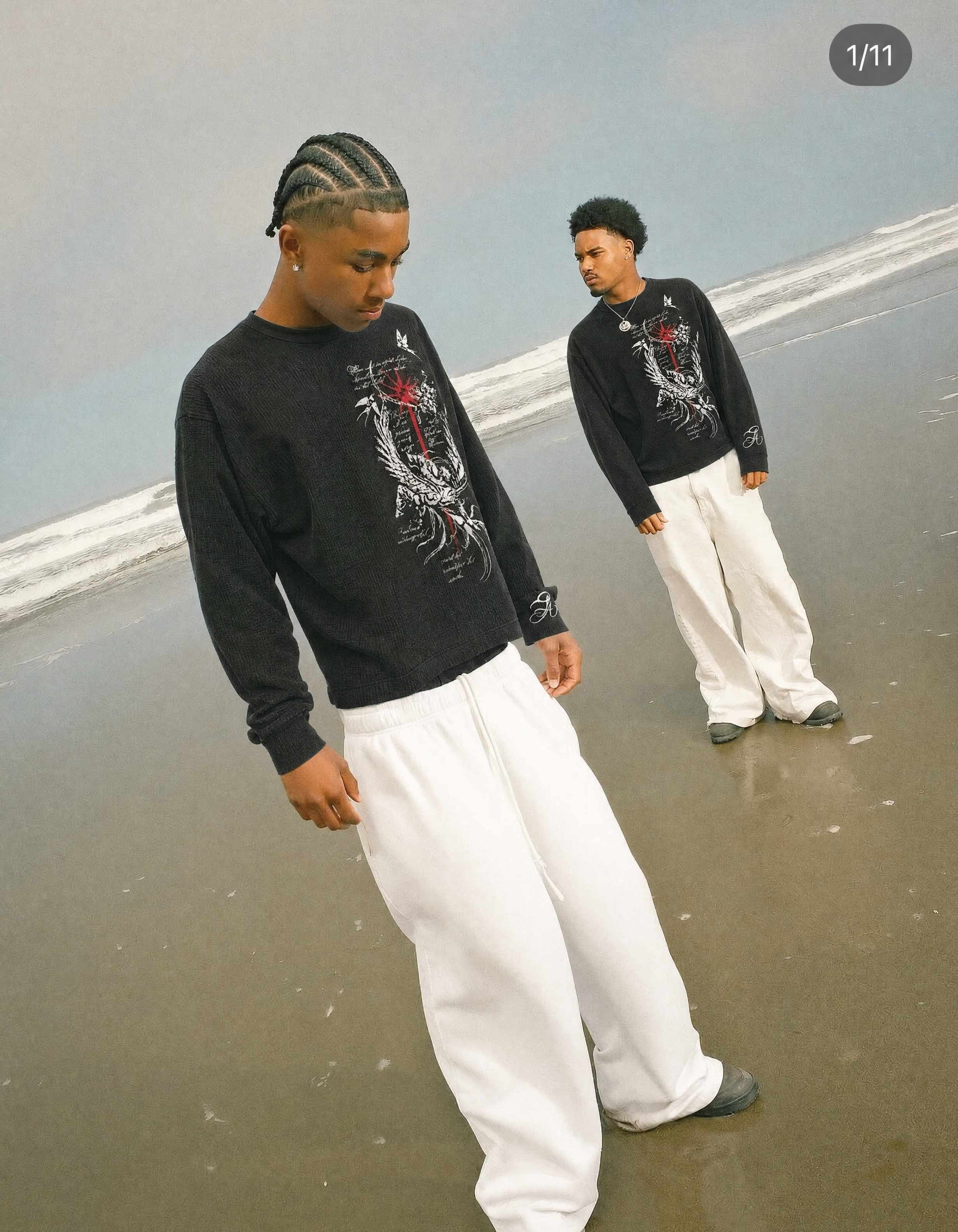 Two models on a beach wearing black graphic long-sleeve shirts and white pants
